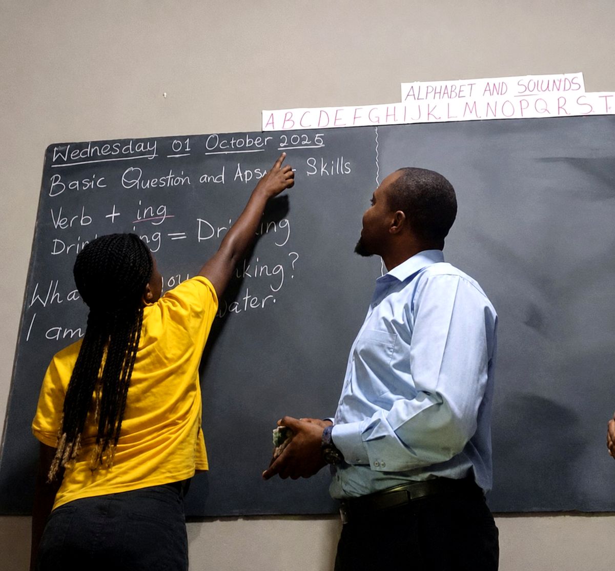 A student points out the alphabet at the chalkboard during an English lesson